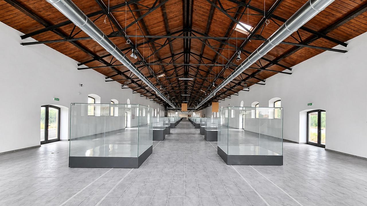 Ampio salone con soffitto a capriate in legno e travi in acciaio. Due file di teche in vetro su basi grigie disposte lungo la navata centrale. Pavimento in piastrelle grigie, finestre ad arco sui lati.